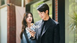 Boy is smiling while texting to someone and girl has a shocked expresion looking at him smiling.
